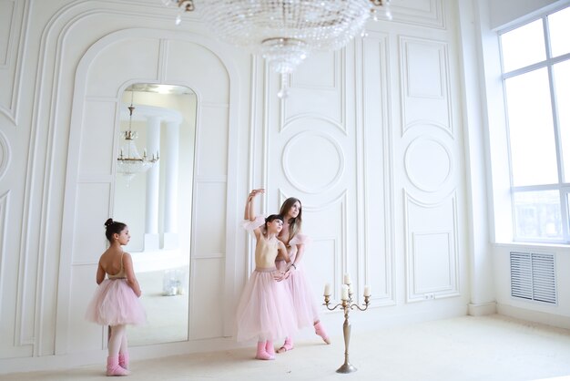 Leraar traint ballet bewegingen met kleine meisjes in roze kleding in de kamer