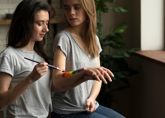 Gratis foto lesbische vrouw die de regenboogvlag op de hand van haar meisje met penseel schildert