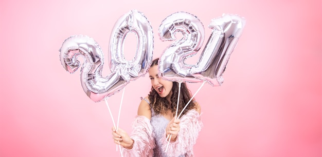 Leuk jong meisje met een glimlach in een feestelijke outfit poseren tegen een roze studio achtergrond en houdt zilveren ballonnen voor het nieuwe jaar concept