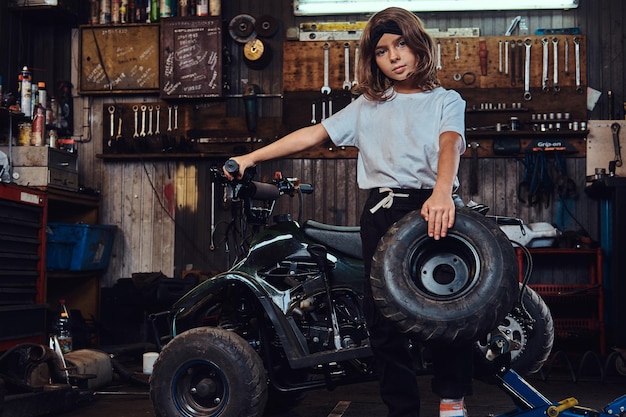 Leuk klein meisje poseert voor fotograaf met groot wiel van kapotte atv bij autoservice.