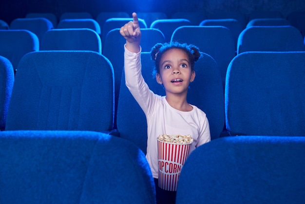 Leuk meisje die met vinger poiniting bij het scherm in bioskoop.