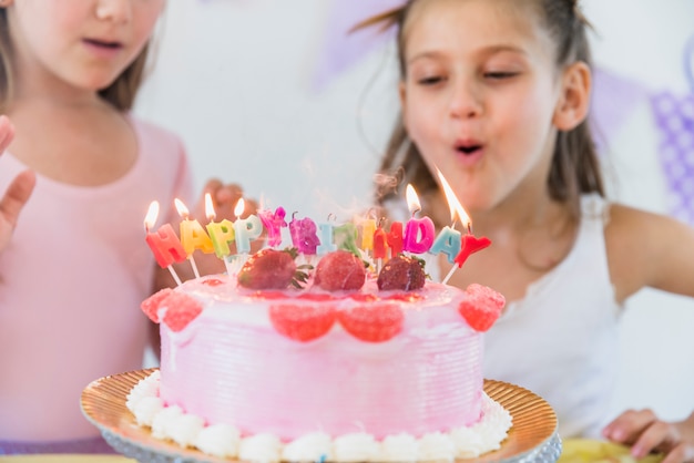 Gratis foto leuk meisje die multicolored kaarsen op verjaardagscake blazen