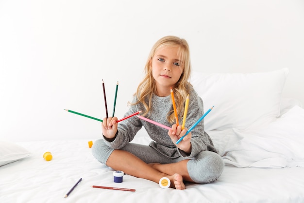 Leuk meisje in grijze pyjama's die haar kleurrijke potloden in slaapkamer tonen