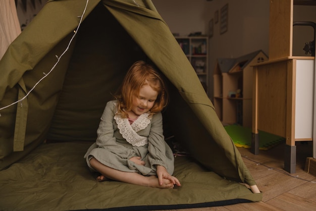 Gratis foto leuk meisje met een lichte huid en rood haar zit in een groene tent in de kinderkamer babyconcept