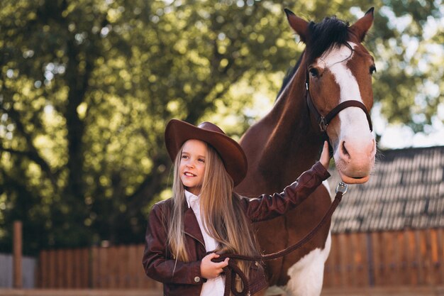 Leuk weinig blondemeisje met paard bij boerderij
