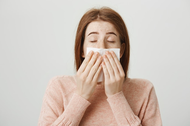 Leuk ziek roodharigemeisje met allergie die in servet niezen