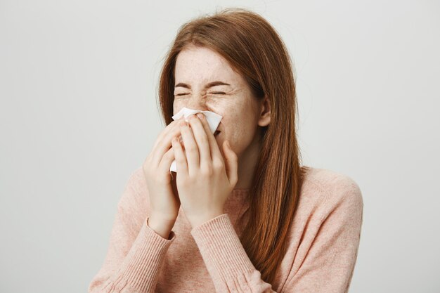 Leuk ziek roodharigemeisje met allergie die in servet niezen