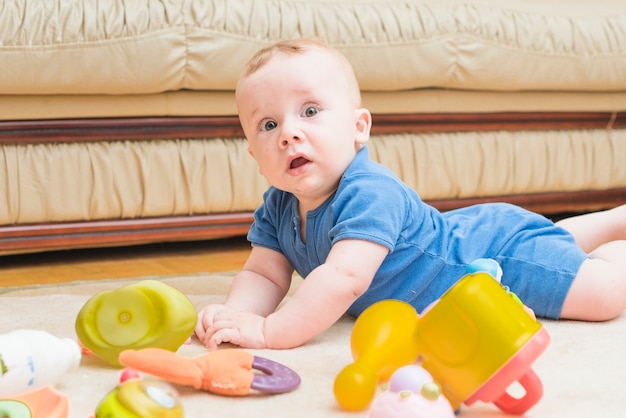 Leuke babyjongen die op tapijt met speelgoed legt