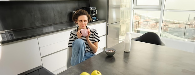 Leuke brunette vrouw student ontbijt in de ochtend drinken warme thee glimlachen en kijken tevreden