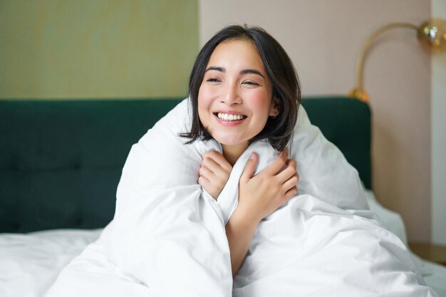 Leuke en tedere vrouw die in bed zit met een warm dekbed glimlachend terwijl ze uit het raam kijkt en geniet van m