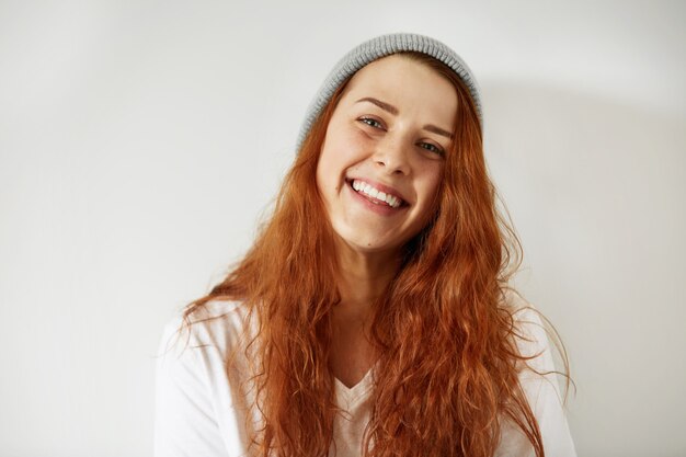 Leuke gelukkige jonge vrouw in grijze pet en wit T-shirt kijken en glimlachen