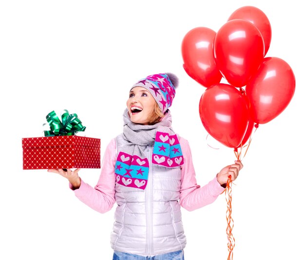 Leuke gelukkige volwassen vrouw met rode giftdoos en ballons die omhoog geïsoleerd op wit kijken