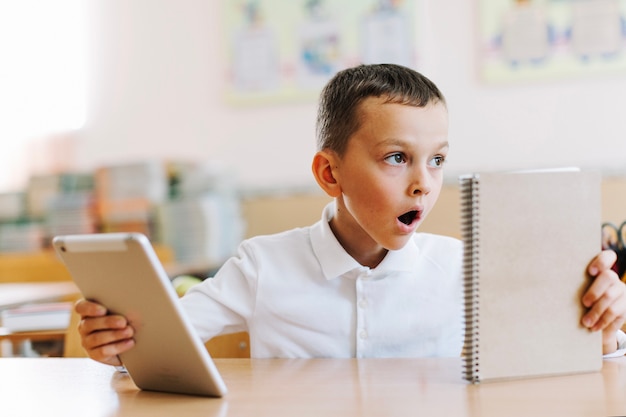 Leuke geschokte jongen met tablet en notitieblok