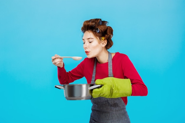 Leuke huisvrouw ruikt en proeft warme zelfgemaakte soep in de keuken