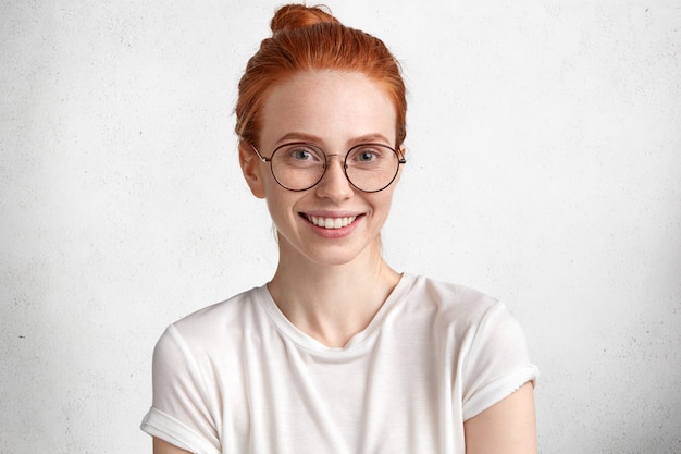 Gratis foto leuke intelligente roodharige vrouwelijke student in ronde bril, verheugt zich met succes geslaagd voor examen in vreemde talen