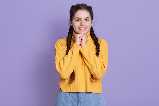 Leuke jonge jonge vrouw met charmante glimlach, die camera bekijkt en vuisten onder kin houdt