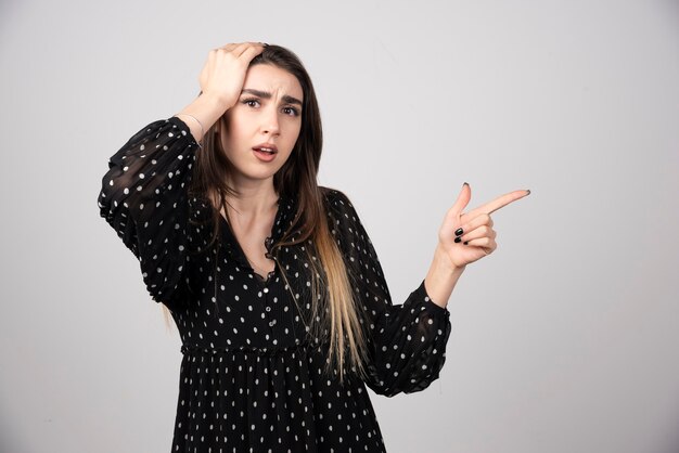 Leuke jonge vrouw die een vinger wegwijst op een grijze muur.