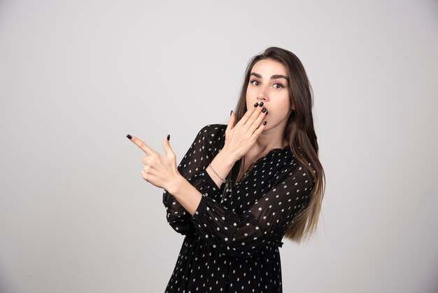 Leuke jonge vrouw die een vinger wegwijst op een grijze muur.