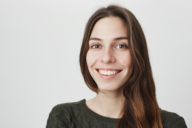 Leuke jonge vrouw die met witte tanden glimlacht, kijkt gelukkig