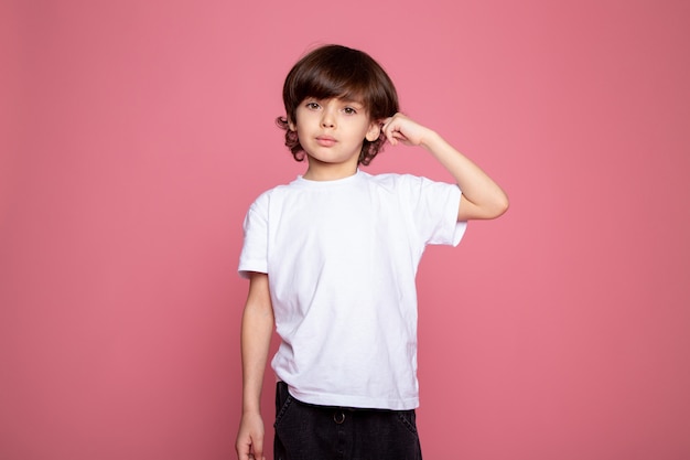 Leuke jongen weinig in het witte t-shirt en jeansportret op roze bureau