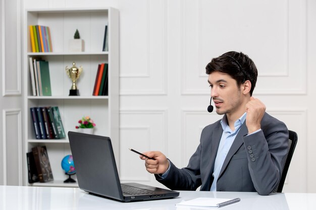 Leuke kerel van de klantenservice in grijs pak met computer en headset die vuisten vasthoudt