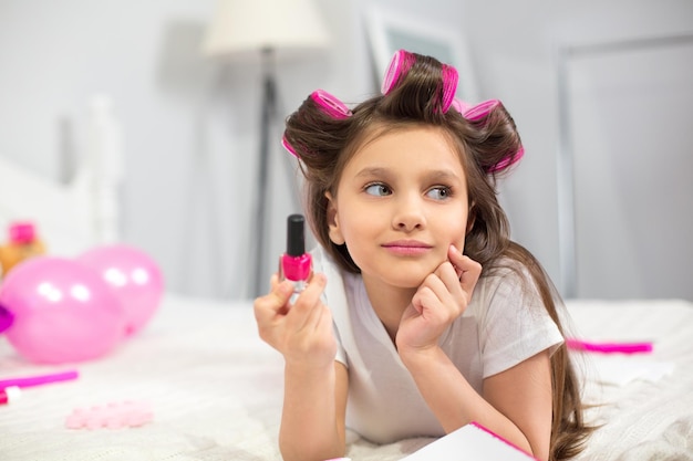 Leuke kleuter die op witte deken legt die nagellak houdt.