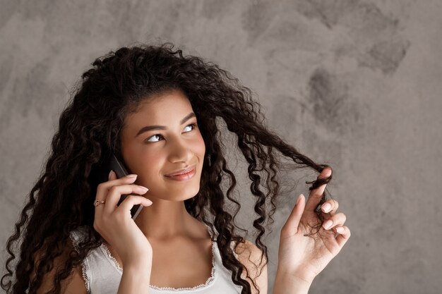 Leuke krullende vrouw die op telefoon spreekt, rolt haar streng op vinger