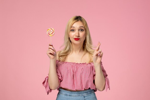Leuke meisjes mooie jonge dame met rode lippenstift in roze blouse die vingers kruist met lolly