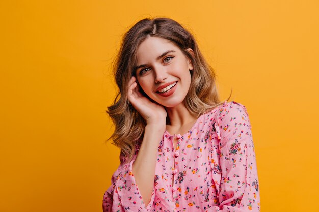 Leuke mooie vrouw met golvend haar lachen op gele muur. Binnenfoto van vrij wit meisje draagt roze blouse.