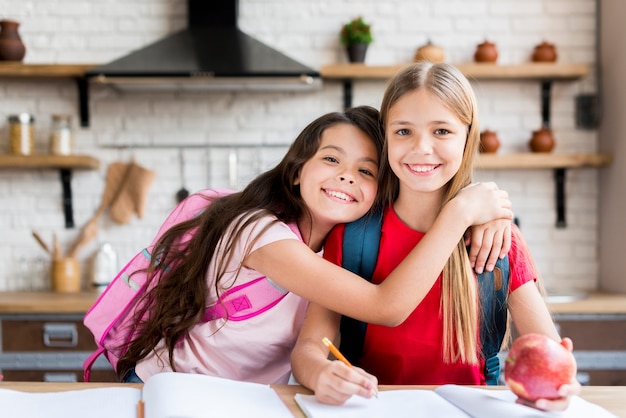 Gratis foto leuke schoolkinderen met rugzakken die bij lijst zitten en thuiswerk doen