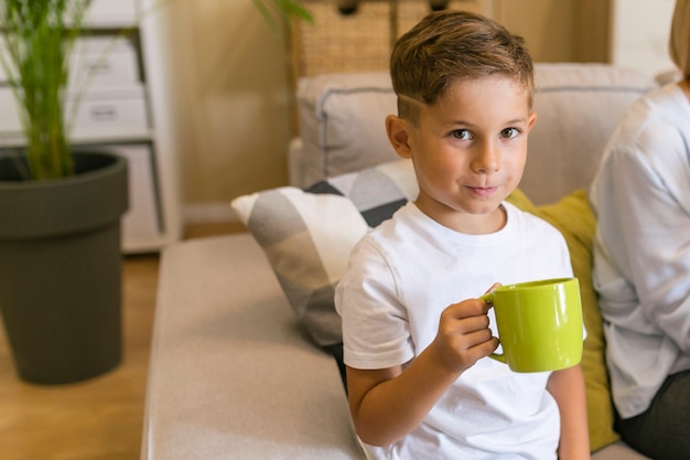 Gratis foto leuke smiley kleine jongen die een gele mok houdt