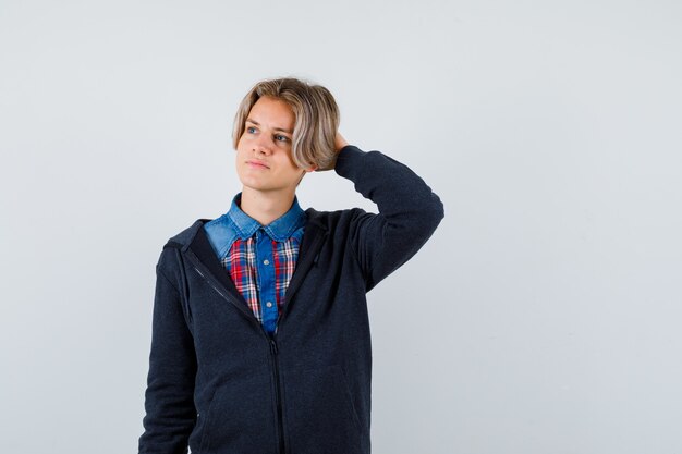 Leuke tienerjongen die de hand achter het hoofd houdt, wegkijkt in shirt, hoodie en peinzend kijkt. vooraanzicht.