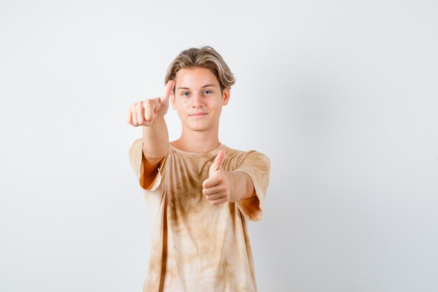 Leuke tienerjongen die dubbele duimen in t-shirt toont en er tevreden uitziet, vooraanzicht.