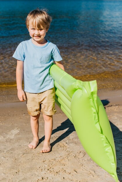 Leuke vrolijke jongen met opblaasbare matras op strand