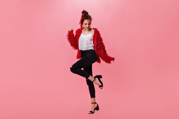 Leuke vrouw in wollen jas en zwarte broek dansen op roze