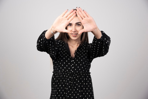 Leuke vrouw in zwarte jurk die driehoek op grijs maakt.