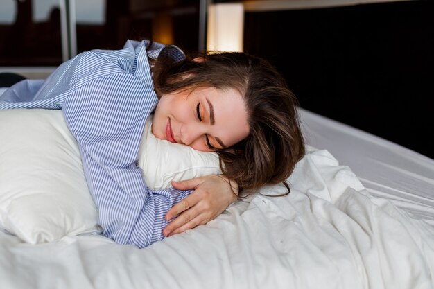 Leuke vrouw liggend op haar buik op het bed en slaap. Stijlvolle zwarte lingerie en gestreept boyfriend-shirt dragen.