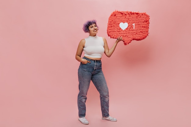 Leuke vrouw met heldere ongebruikelijke haren poseert met een hand in haar zak en een ander vasthoudend teken zoals op roze