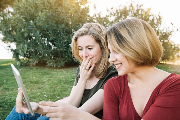 Gratis foto leuke vrouwen die tablet in park doorbladeren