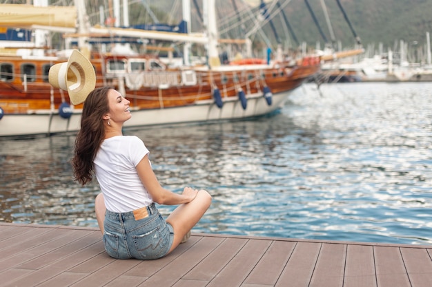 Gratis foto leuke vrouwenzitting op de kust van een haven