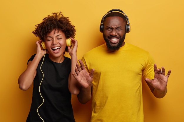 Levendig energiek paar met donkere huid dansen en hebben samen plezier, luister naar verschillende soorten muziek in koptelefoons geïsoleerd op een lichte achtergrond.