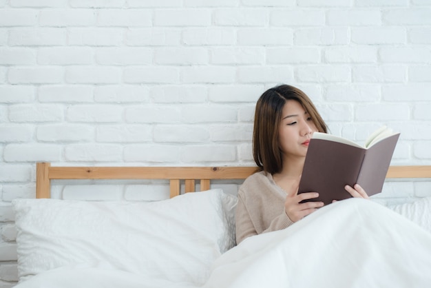 Levensstijl gelukkige jonge Aziatische vrouw genieten van liggend op het bed lezen boek plezier in casual kleding