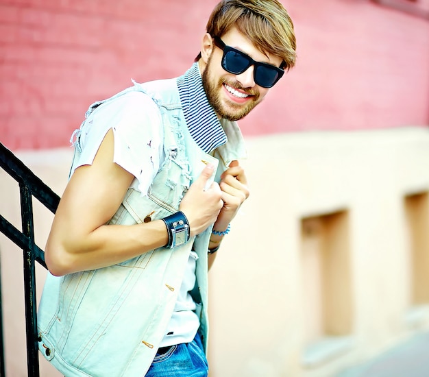 Levensstijlportret van grappige glimlachende hipster knappe mensenkerel in modieuze de zomerkleren die op straatachtergrond stellen in zonnebril