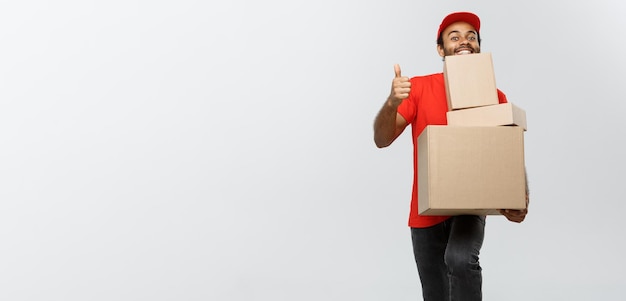 Levering Concept Portret van gelukkige Afro-Amerikaanse bezorger die doospakketten vasthoudt en bonzen laat zien. Geïsoleerd op grijze studio-achtergrond Kopieer ruimte