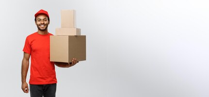 Levering concept portret van gelukkige afro-amerikaanse bezorger in rode doek met een doos pakket geïsoleerd op grijze studio achtergrond kopie ruimte