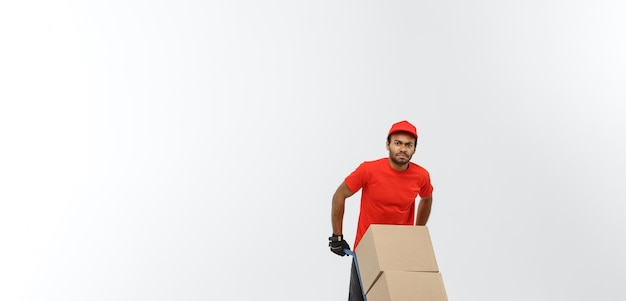 Levering Concept portret van knappe Afro-Amerikaanse bezorger of koerier duwen steekwagen met stapel dozen geïsoleerd op grijze studio achtergrond kopie ruimte