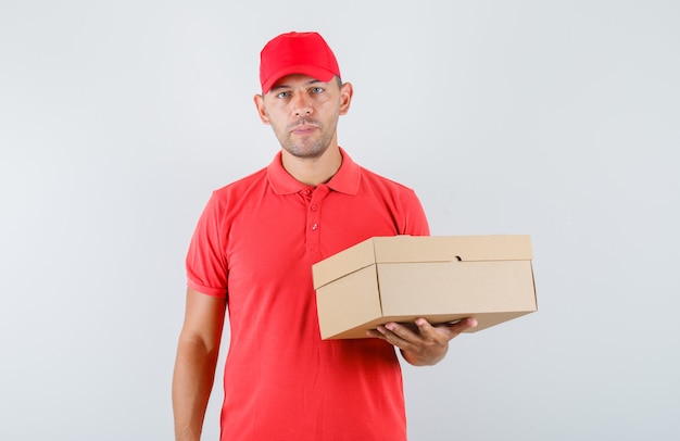 Levering man in rode pet en t-shirt met kartonnen doos en op zoek zelfverzekerd