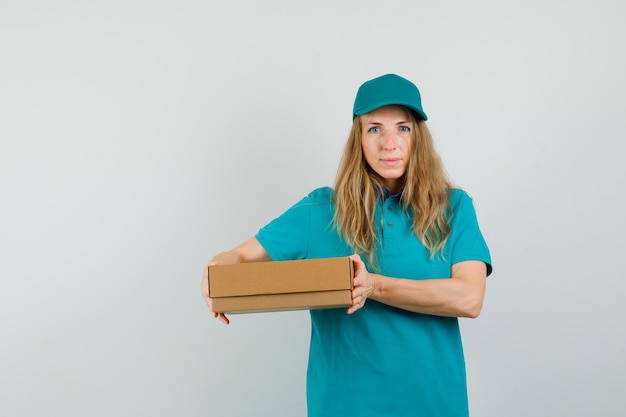 Levering vrouw in t-shirt, pet met kartonnen doos en glimlachen