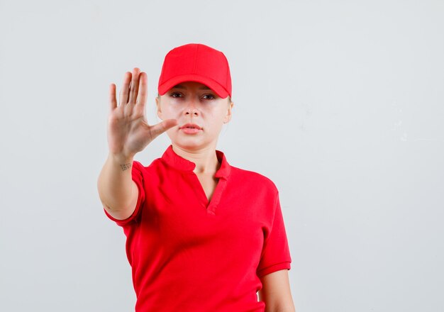 Levering vrouw stop gebaar in rood t-shirt en pet tonen en streng kijken