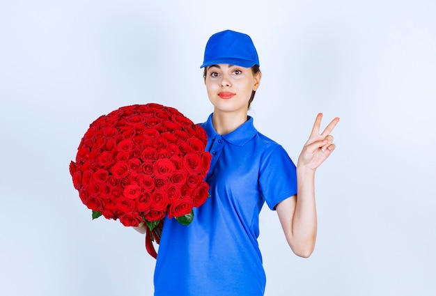 Levering vrouw werknemer in uniform met boeket rozen met overwinningsteken.